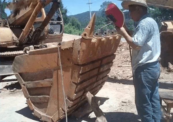 a mechanic is welding bucket teeth for an excavator bucket
